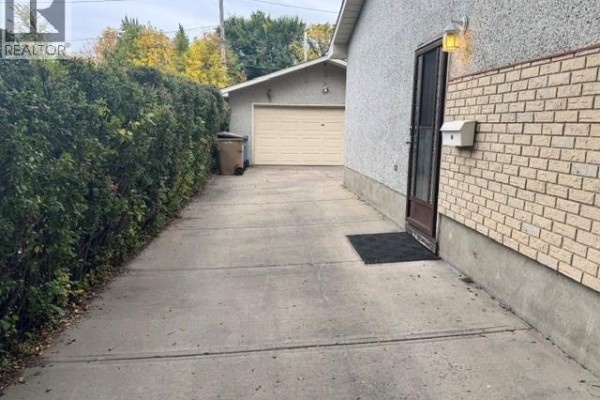 Concrete driveway running alongside a hedge, leading to a detached garage. - 147 Woodward Avenue, Regina