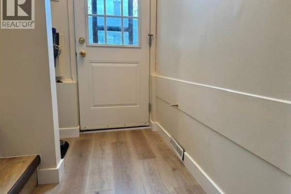 Interior view of a hallway with a white door and light wood laminate flooring. - 147 Woodward Avenue, Regina