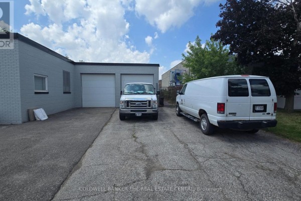 Rear exterior of commercial building showing two large garage doors and parked vans. - 1471 Wallace Road, Oakville
