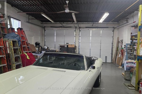 Interior view of a commercial garage with two white overhead doors and a classic car. - 1471 Wallace Road, Oakville