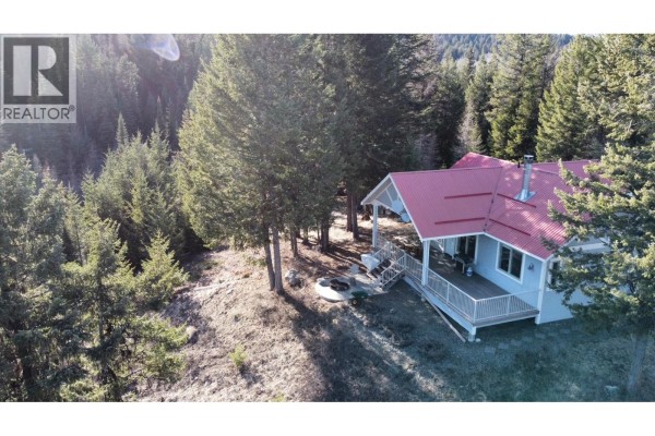 Aerial view of a light blue house with a red metal roof and wraparound deck surrounded by trees. - 1475 Courtenay Brown Road, Bridesville
