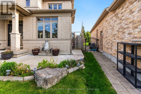 A walkway leads past a concrete patio and decorative rocks to a black metal gate. - 1479 Sandpiper Drive E, London North