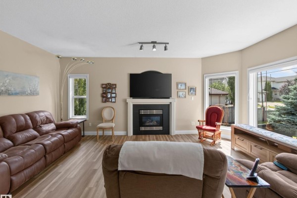 Living room with a brown leather sofa, electric fireplace with a black mantel, and large windows. - 148 Forrest Dr, Sherwood Park