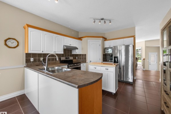 Kitchen with white cabinets, dark brown tile floors, stainless steel refrigerator, and a dark countertop. - 148 Forrest Dr, Sherwood Park