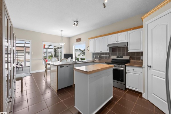 Kitchen with white cabinets, dark brown tile floors, a stainless steel gas stove, and a window view. - 148 Forrest Dr, Sherwood Park