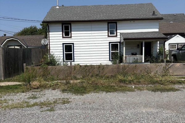 Side view of a white house with white horizontal siding and a covered front porch with a railing. - 148 Kinnear Street, Port Colborne