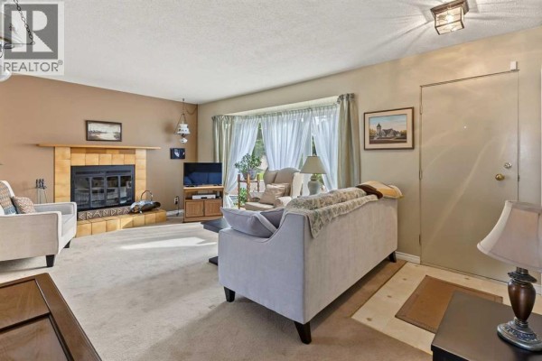 Living room with a beige carpet, fireplace, and a large bay window with sheer curtains. - 148 Marwood Circle Ne, Calgary