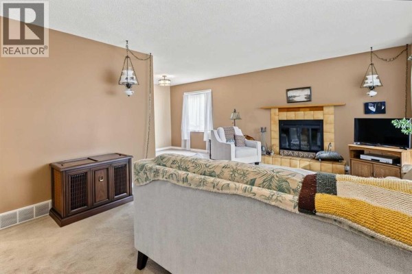 Living room with a fireplace, wood cabinet, and beige carpet. - 148 Marwood Circle Ne, Calgary