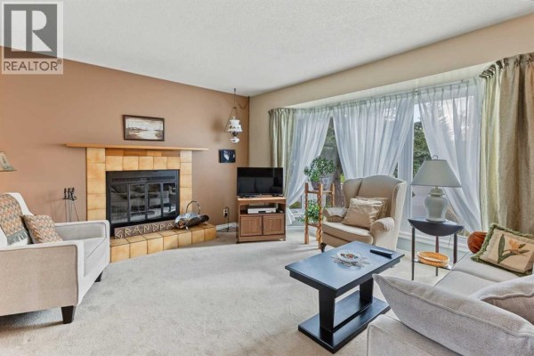 Living room featuring a corner fireplace, seating area, and a large bay window. - 148 Marwood Circle Ne, Calgary