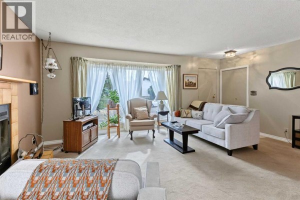 Living room with a fireplace, sofa, armchair, and a bay window overlooking the exterior. - 148 Marwood Circle Ne, Calgary