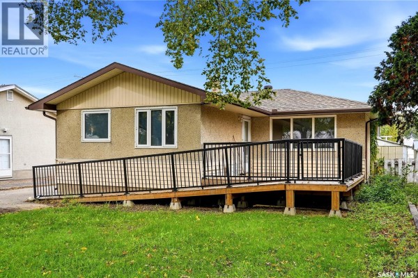 Rear exterior of house with green lawn, wooden deck with black railings, and a long accessible ramp. - 148 Woodward Avenue, Regina