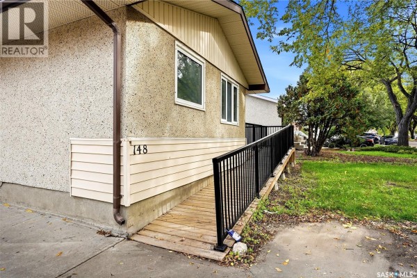 Close-up of house exterior with beige siding, stucco, and a wooden ramp with black railings. - 148 Woodward Avenue, Regina