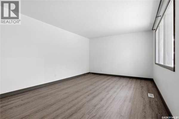 Empty room with white walls, dark wood-look vinyl flooring, and a large window on the right side. - 148 Woodward Avenue, Regina