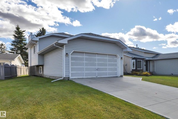 Side exterior view of a light blue house with a double garage door and green lawn. - 14819 35 St Nw, Edmonton