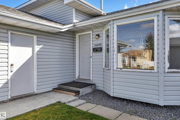 Close-up of the front entrance with a light blue door, bay window, and garage side door. - 14819 35 St Nw, Edmonton