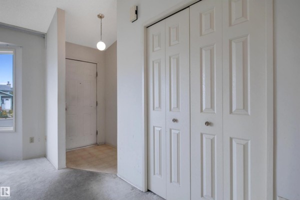 Interior hallway view with a white bi-fold closet door, entry door, and pendant light. - 14819 35 St Nw, Edmonton