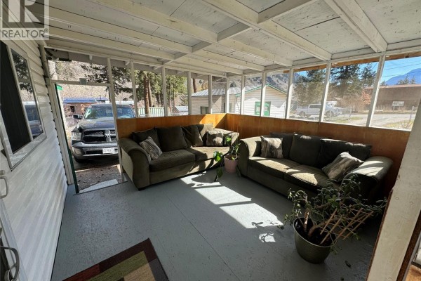 Screened-in sunroom with two large green sofas, plants, and views of the property. - 1483 Main Street, Olalla