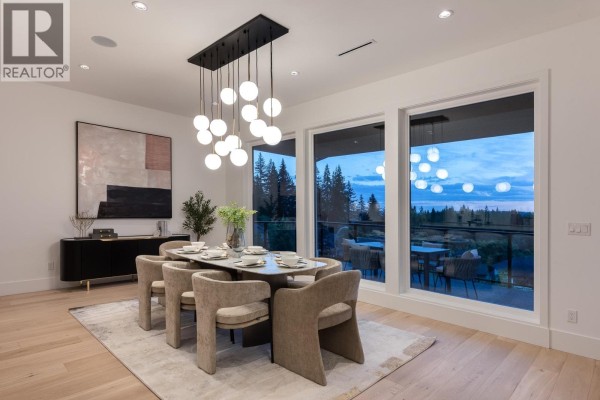 Dining room with a contemporary chandelier and wide windows overlooking trees. - 1484 Copper Beech Place, Coquitlam