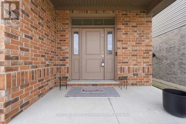 Close-up of the front door with sidelights, framed by red brick and a concrete porch. - 1485 Riverbend Road, London South