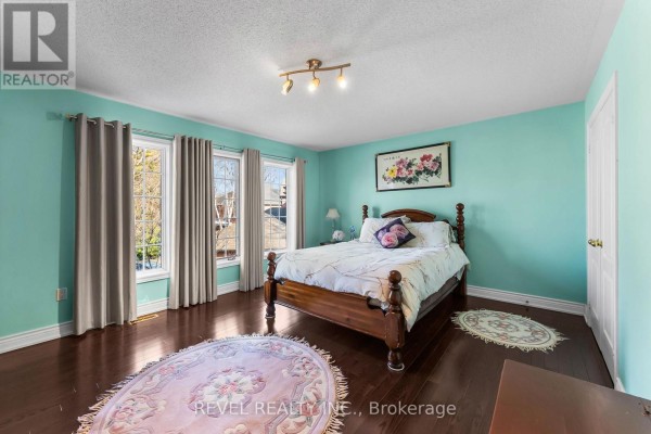 Bedroom with wood bed, teal walls, hardwood floors, floral rug and three windows - 1486 Ashwood Gate Pickering
