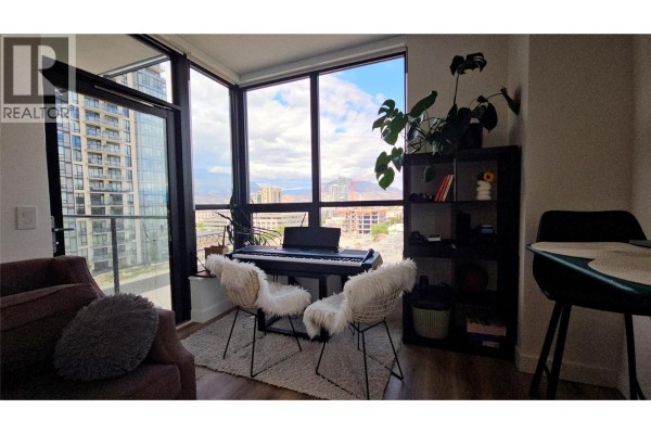 Corner of a living space with large windows, a keyboard, and two decorative chairs. - 1488 Bertram Street Unit# 1008, Kelowna