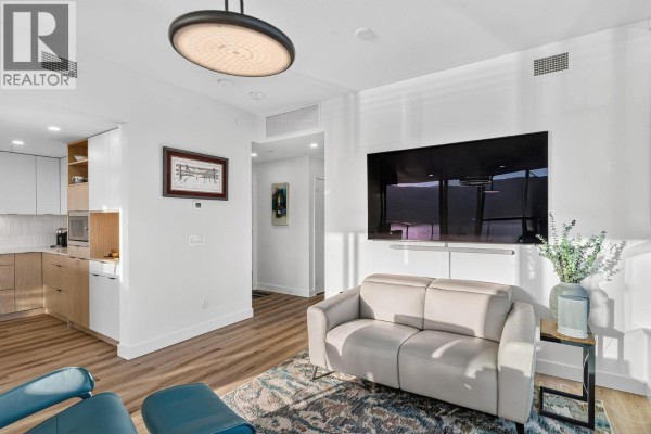Living room showing a sofa, television, and a modern kitchen with light wood cabinetry and white tile backsplash. - 1488 Bertram Street Unit# 3202, Kelowna