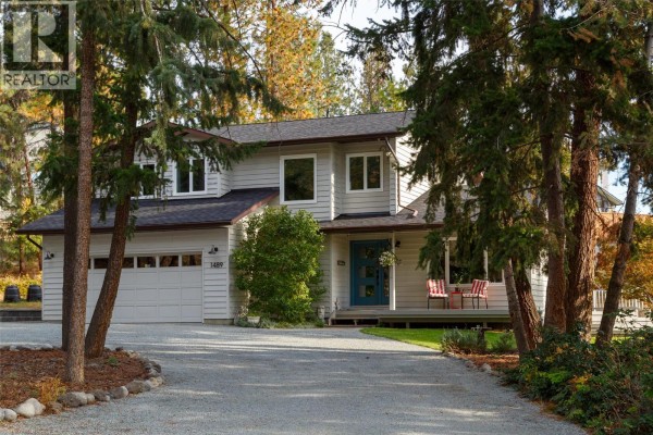 Front view of the house with a gravel driveway leading to the garage and a porch with chairs. - 1489 Bear Creek Road, West Kelowna