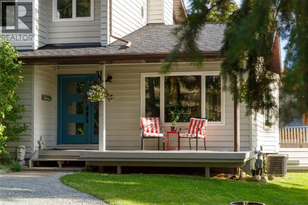 Close-up of the front entrance showing a light grey wood siding, a teal front door, and a small porch. - 1489 Bear Creek Road, West Kelowna