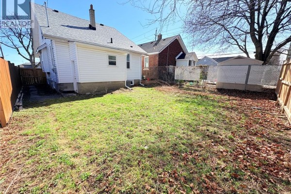 View of the side and backyard of a white house with a wooden fence and shed. - 1489 Windermere Road, Windsor