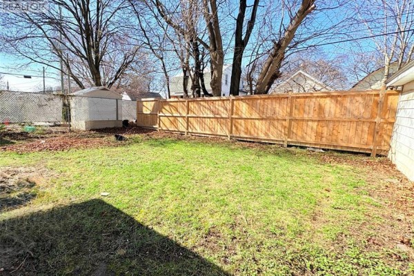 Backyard view with a wooden fence, chain-link fence, shed, and mature trees in the background. - 1489 Windermere Road, Windsor