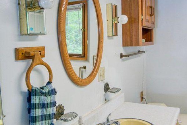 Bathroom vanity with yellow sink, oval mirror, and wooden cabinet - 148b Oak Shores Lane Frontenac