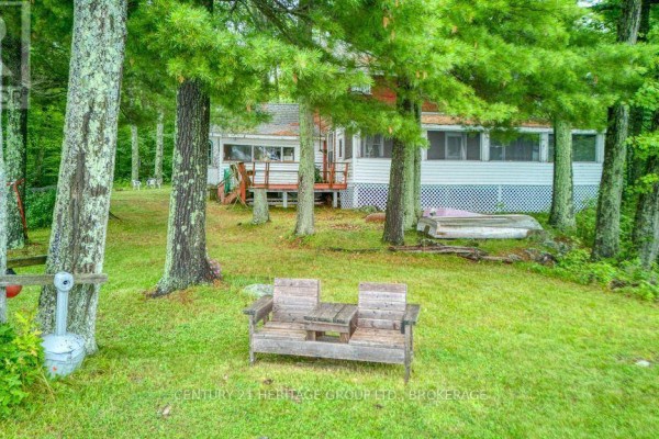 Rustic wooden bench and boat in yard with white cottage and trees - 148b Oak Shores Lane Frontenac
