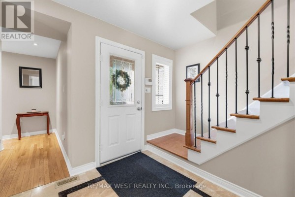 Foyer with white door, hardwood floors, and a staircase with wooden steps and black spindles. - 149 Deerglen Terrace, Aurora