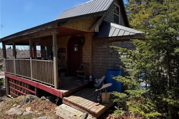 Front view of a wooden cabin with a red door, a covered porch, and a blue water barrel on the side. - 149 Limekiln Road, Letang