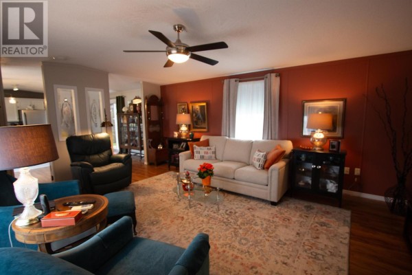 Living room featuring a sofa, armchairs, patterned rug, and an orange accent wall. - 149 Ryan Street, Summerside