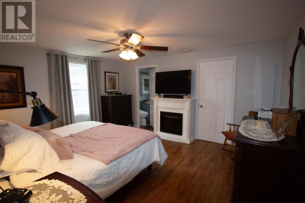 Bedroom with a queen-size bed, electric fireplace, dresser, and attached bathroom entrance. - 149 Ryan Street, Summerside