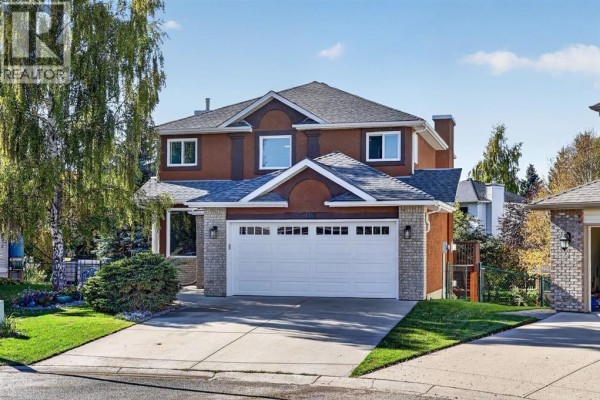 Exterior view of a two-story house with a double garage, showcasing brick and stucco details. - 149 Valley Ridge Court Nw, Calgary