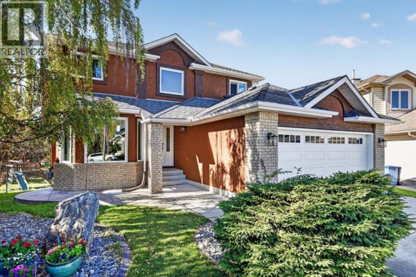 Front exterior of a house with a landscaped yard, featuring a large stone and dense green shrubs. - 149 Valley Ridge Court Nw, Calgary