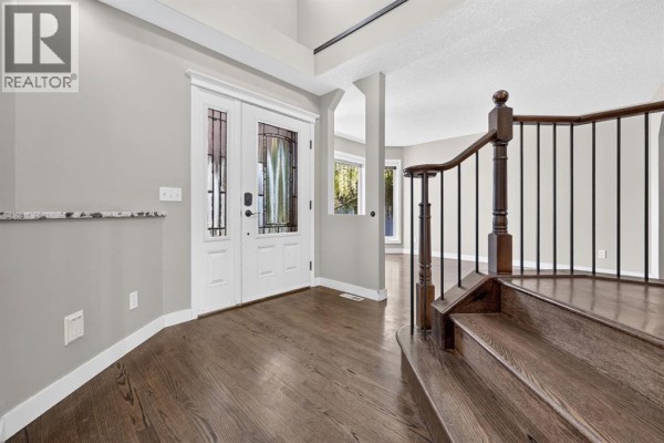 Foyer with double white doors, hardwood floors, and a dark wood staircase with metal spindles. - 149 Valley Ridge Court Nw, Calgary