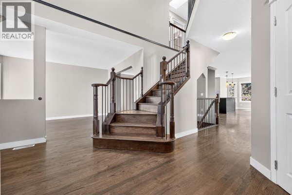 Wide view of a foyer and staircase with dark hardwood floors and neutral walls, leading to open living areas. - 149 Valley Ridge Court Nw, Calgary