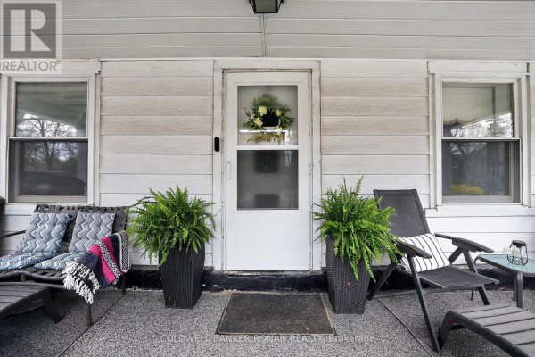 Front door with a window, flanked by ferns and outdoor seating on a porch. - 149 Victoria Street W, New Tecumseth
