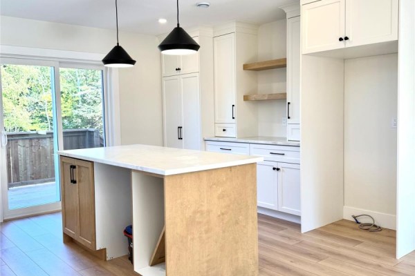 View of the kitchen island, white cabinets, and sliding glass doors leading to an outdoor deck. - 1490 Thorburn Road, St  Philip’s