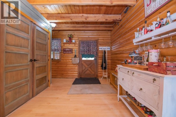 Log cabin kitchen with island, range, cabinets, and wood-paneled walls and ceiling. - 1495 6 Highway, Nakusp