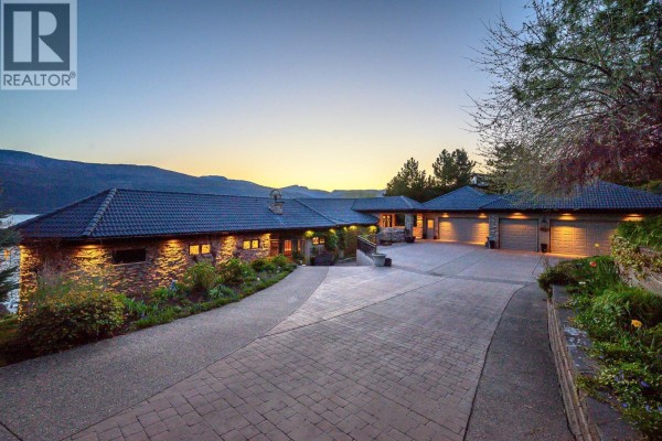 Beachfront view of a large house on a rocky hillside with a dock and seating area. - 14966 Carrs Landing Road, Lake Country