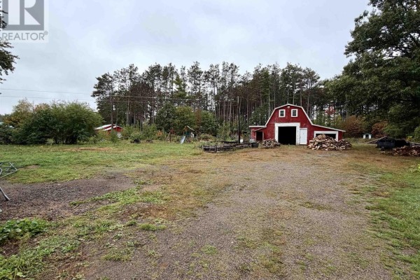 View of a large red barn with open doors and woodpile, surrounded by trees. - 14967 Highway 1, Wilmot