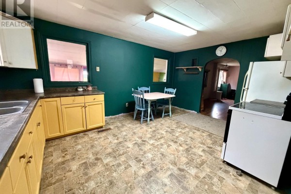 Kitchen with dark green walls, yellow cabinets, white appliances, and a small table with blue chairs. - 14967 Highway 1, Wilmot