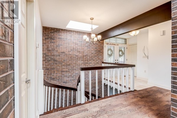 Interior staircase with a brick accent wall, wood railing, and skylight above. - 1499 Ashington Court, Mississauga