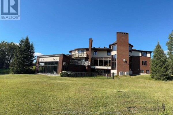 Another rear view of the house with a prominent brick chimney and a large glass-enclosed room. - 1499 Kraft Creek Road, Timmins