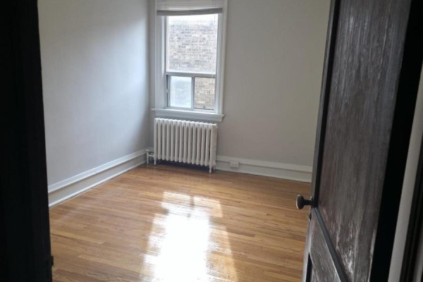 Empty bedroom with hardwood floors, white walls, and window with radiator. - 15 - 35 Jane Street, Toronto