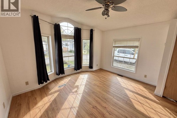 Interior view of a living room with bay windows, blinds, and wood laminate flooring. - 15 3211 Gook Road, Quesnel